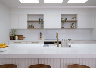 Modern minimalist kitchen with white cabinets, wood stools, and skylights.