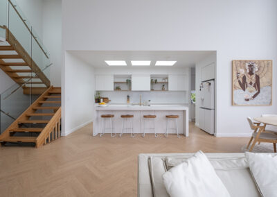 Modern minimalist kitchen with white cabinets, wood stools, and skylights.