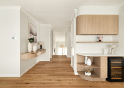 Modern white kitchen with a curved island, gold fixtures, built-in ovens, and an outdoor BBQ area