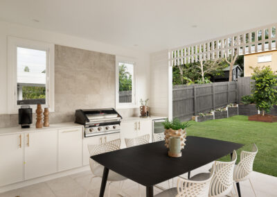 Modern white kitchen with a curved island, gold fixtures, built-in ovens, and an outdoor BBQ area