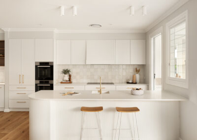 Modern white kitchen with a curved island, gold fixtures, built-in ovens, and an outdoor BBQ area