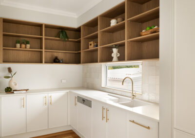 Modern white kitchen with a curved island, gold fixtures, built-in ovens, and an outdoor BBQ area