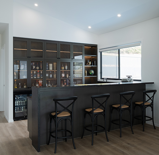 Custom home bar with mesh display cabinetry, stone benchtop, bar seating and under-bench fridge by Zente Kitchens