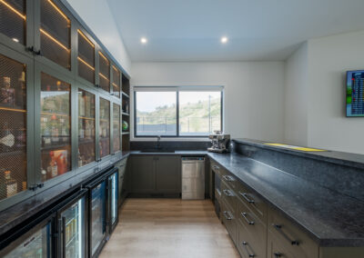 Full view of custom home bar with display cabinetry, bar fridges, sink and stone benchtop