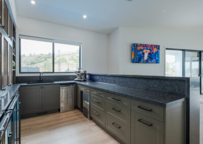 Custom home bar with mesh display cabinetry, bar fridges, stone benchtop and seating by Zente Kitchens
