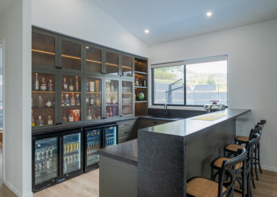 Custom home bar with mesh display cabinetry, bar fridges, stone benchtop and seating by Zente Kitchens