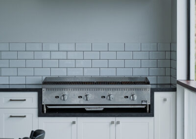 Built-in outdoor BBQ with white shaker cabinetry, tiled splashback and stainless rangehood