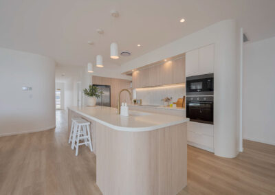 Coastal kitchen with curved Formica Soft Oak island, Better White stone and integrated appliance cabinetry