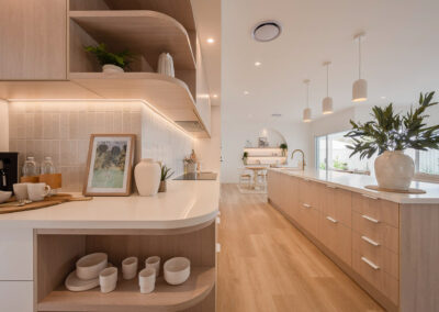 Soft Oak kitchen cabinetry with curved shelves, white stone and island beyond