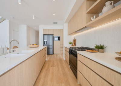 Galley kitchen with Laminex Aged Ash cabinetry, white benchtops and integrated black appliances