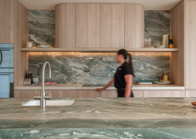 Custom coastal kitchen with stone island, integrated sink, feature stone splashback and timber-look cabinetry