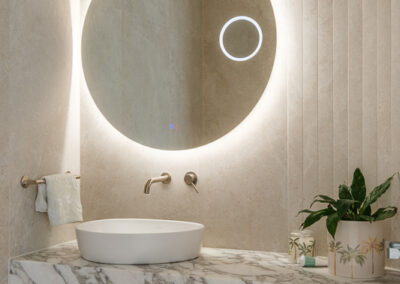 Custom bathroom vanity with round backlit mirror, stone benchtop and timber-look drawers