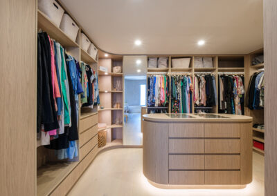Walk-in robe with custom timber-look cabinetry, island drawers and open hanging storage