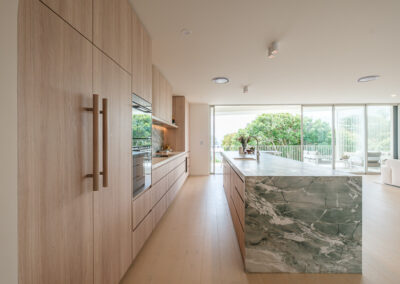 Galley-style coastal kitchen with integrated appliance wall, stone island and timber-look cabinetry