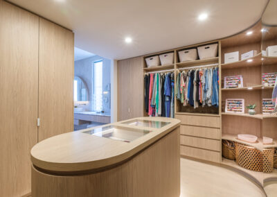 Walk-in robe island with curved cabinetry, hanging storage and timber-look finishes