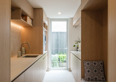 Custom laundry with timber-look cabinetry, long benchtop, open shelving and garden outlook