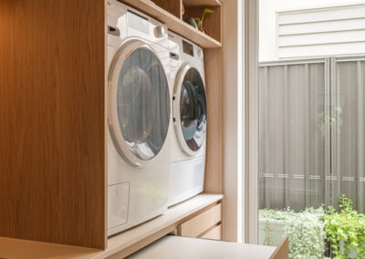 Stacked laundry appliances with custom cabinetry and pull-out bench