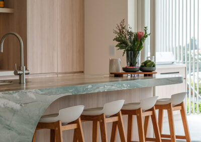 Curved stone kitchen island with timber stools, sink and coastal cabinetry by Zente Kitchens