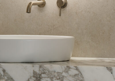 Bathroom vanity close-up with round backlit mirror, countertop basin and stone benchtop