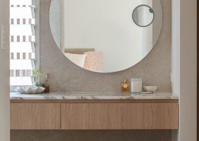 Bathroom vanity close-up with round backlit mirror, countertop basin and stone benchtop